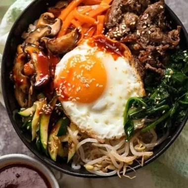A colorful bowl of bibimbap with vegetables, rice, and an egg, showcasing Korean cuisine.
