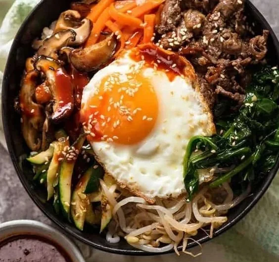 A colorful bowl of bibimbap with vegetables, rice, and an egg, showcasing Korean cuisine.
