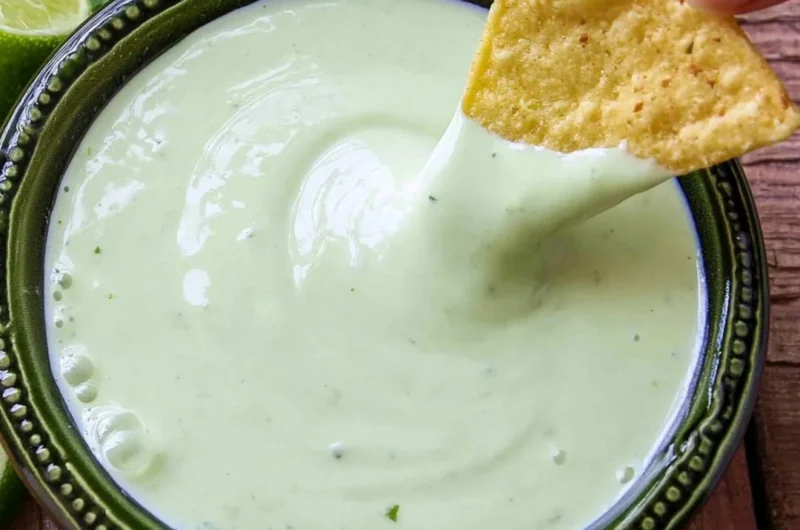 Fresh cilantro lime cream in a bowl with herbs and lime slices
