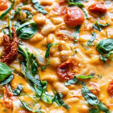 Bowl of creamy vegan tomato white bean stew garnished with herbs