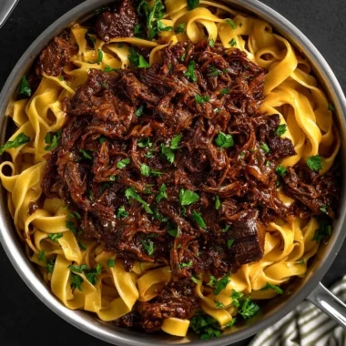 Delicious slow-cooked short rib ragù served over pasta, garnished with herbs.
