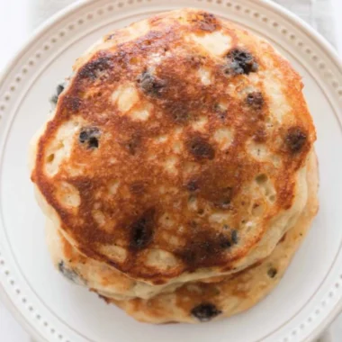 Fluffy sourdough pancakes stacked on a plate with syrup and berries