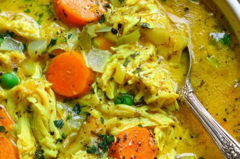 Bowl of chicken soup with turmeric and ginger, garnished with fresh herbs.