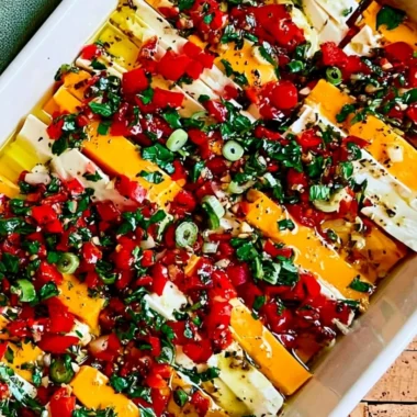 A bowl of marinated cheese with herbs and spices on a rustic wooden table