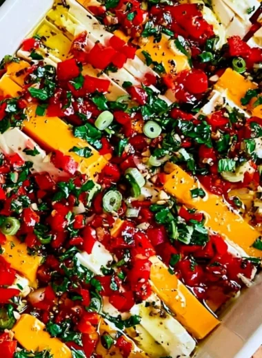 A bowl of marinated cheese with herbs and spices on a rustic wooden table